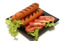 Roast sausages on black dish with lettuce and slic