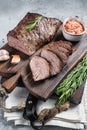 Roast and sliced tri tip beef steak on a wooden board with herbs. Gray background. Top view Royalty Free Stock Photo