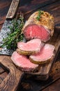 Roast Tenderloin beef fillet meat on a wooden board with herbs. Dark wooden background. Top view