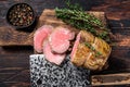 Roast Tenderloin beef fillet meat on a wooden board with herbs. Dark wooden background. Top view