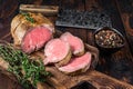 Roast Tenderloin beef fillet meat on a wooden board with herbs. Dark wooden background. Top view