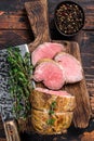 Roast Tenderloin beef fillet meat on a wooden board with herbs. Dark wooden background. Top view
