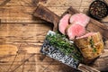 Roast Tenderloin beef fillet meat on a wooden board with herbs. Dark wooden background. Top view. Copy space