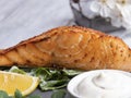 Roasted baked salmon fillet with lemon, white sauce and spinach, close up