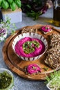 Roasted beet hummus in ceramic bowl, flax seed crackers on wooden cutting board, pesto sauce jar - vegetarian, vegan food concept