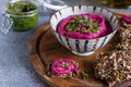 Roasted beet hummus in ceramic bowl, flax seed crackers on wooden cutting board, pesto sauce jar - vegetarian, vegan food concept