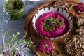 Roasted beet hummus in ceramic bowl, flax seed crackers on wooden cutting board, pesto sauce jar - vegetarian, vegan food concept