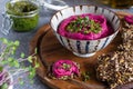 Roasted beet hummus in ceramic bowl, flax seed crackers on wooden cutting board, pesto sauce jar - vegetarian, vegan food concept