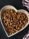 Roasted cashew nuts on a heart-shaped plate on a dark background, vertical shot, top view Royalty Free Stock Photo