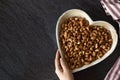 Roasted cashew nuts on a heart-shaped plate with a human hand holding it on a dark background with copy space Royalty Free Stock Photo