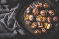 Roasted chestnuts in iron grilling pan with kitchen napkin over rustic wooden board, top view