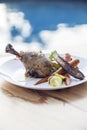 Roasted chicken leg, with carrots, tomato and zuquini served on a white plate by the pool Royalty Free Stock Photo