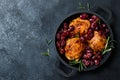 Roasted chicken legs with red grapes on pan over black slate stone background. Royalty Free Stock Photo