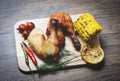 Roasted chicken legs on wooden cutting board with corn lemon chilli spicy herbs spices and tomato on dining table food - Grilled Royalty Free Stock Photo