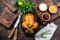 Roasted chicken with rosemary served on black plate with sauces on wooden table, top view.