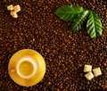 Roasted coffee beans background white cup on golden saucer with foamy espresso, top view. On beans fresh green coffee leaves, Royalty Free Stock Photo