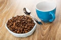 Roasted coffee beans in bowl, spoon, empty coffee cup on wooden table