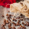 Roasted coffee beans on a brown wooden background with coarse roughly woven burlap and red rose, grunge texture. Place Royalty Free Stock Photo