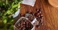 Roasted coffee beans get out of overturned glass jar on wooden background, selective focus, side view