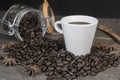 Roasted coffee beans in glass jar with a white coffee cup on vintage table.Closeup view with copy space on dark background Royalty Free Stock Photo