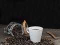 Roasted coffee beans in glass jar with a white coffee cup on vintage table.Closeup view with copy space on dark black background Royalty Free Stock Photo