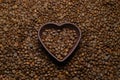 Roasted coffee beans in heart shaped bowl on coffee background. Royalty Free Stock Photo