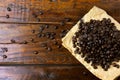 Roasted coffee beans on paper on rustic wooden table, beans around scattered