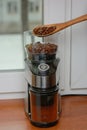 The roasted coffee beans are poured from a wooden spoon into an electric coffee grinder Royalty Free Stock Photo