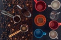 Roasted coffee beans, scoop, coffee pot, coffee tamper and cup of coffee with empty cups on black Royalty Free Stock Photo