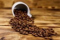 Roasted coffee beans spill out of cup on wooden table Royalty Free Stock Photo