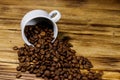 Roasted coffee beans spill out of cup on wooden table Royalty Free Stock Photo