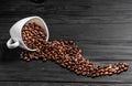 Roasted coffee beans spilling out of a white cup on the wooden table Royalty Free Stock Photo