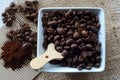 ROASTED COFFEE BEANS IN A WHITE CERAMIC BOWL AND WOODEN SCOOP WITH GROUNDS ON CORRUGATED CARDBOARD AND HESSIAN Royalty Free Stock Photo