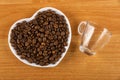 Roasted coffee beans in saucer in heart shape, empty coffeecup on wooden table. Top view Royalty Free Stock Photo