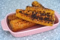 Roasted corn cobs in a pink tray