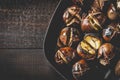 Roasted edible chestnuts in cast iron skillet over rustic wooden table Royalty Free Stock Photo