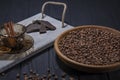 Roasted fragrant grains of black coffee lie in a brown wooden plate which stands on a black wooden table and next to it Royalty Free Stock Photo