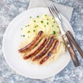 Roasted nuremberg sausages served with sour cabbage and mashed potatoes, on a white plate, top view, square Royalty Free Stock Photo