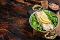 Roasted pollock or coalfish fish fillet served with green salad in a skillet. Wooden background. Top view. Copy space