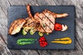 Roasted Pork steak on bone stuffed with cheese, grilled vegetables and berries on stone slate background on wooden background Royalty Free Stock Photo