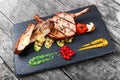 Roasted Pork steak on bone stuffed with cheese, grilled vegetables and berries on stone slate background on wooden background Royalty Free Stock Photo