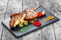 Roasted Pork steak on bone stuffed with cheese, grilled vegetables and berries on stone slate background Royalty Free Stock Photo