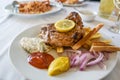 Roasted pork steak with French fries, onions, various dips and a lemon slice, barbecue dish in summer on a white plate, selected