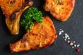 Roasted pork steaks, cutlets with bones and fresh parsley on black stone background, top view