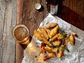Roasted potatoes with herbs on a white paper, a glass of beer on old wooden background, rustic style