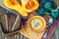 Roasted pumpkin soup with cream, fresh pumpkins and pumpkin seeds in plate on wooden background. Copy space