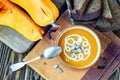 Roasted pumpkin soup with cream, fresh pumpkins and pumpkin seeds in plate on wooden background. Copy space