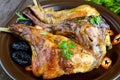 Roasted rabbit leg with prunes on a ceramic plate on dark wooden background.