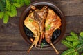 Roasted rabbit leg with prunes on a ceramic plate on dark wooden background with green fir branches.