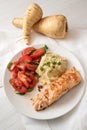 roasted salmon fillet with parsnip mash, tomato salad and parsley garnish, healthy diet dinner on a white plate and a white table